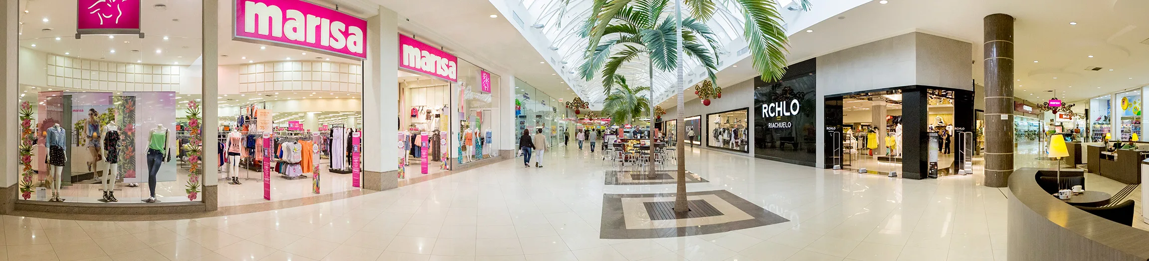 Corredor central do Farol Shopping com palmeiras sob a claraboia